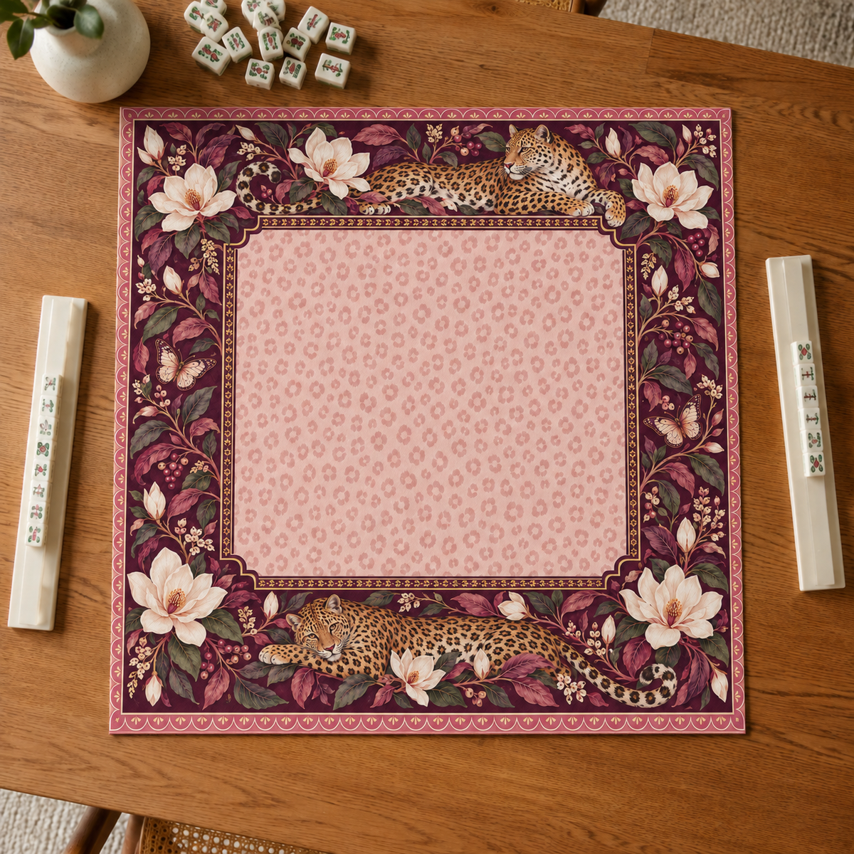Burgundy vegan leather Mahjong mat with leopards and cream magnolias overhead on an oak table
