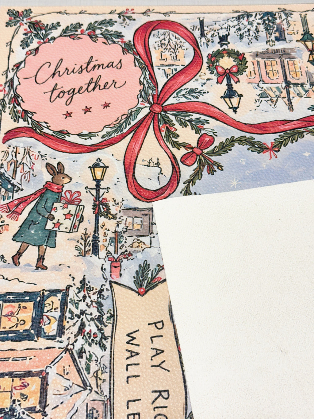 Cream suede backing beside the winter rabbit mat with Christmas together lettering, a red bow and snowy village details