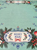 Close-up of Merry Mahj lettering with blue floral flourishes and Christmas greenery on a green Mahjong mat