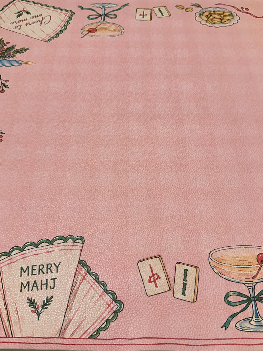 Close-up of a Merry Mahj napkin, cocktail glass and Mahjong tiles on the pink checked Christmas mat
