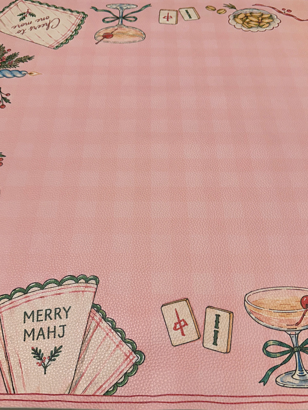 Close-up of a Merry Mahj napkin, cocktail glass and Mahjong tiles on the pink checked Christmas mat