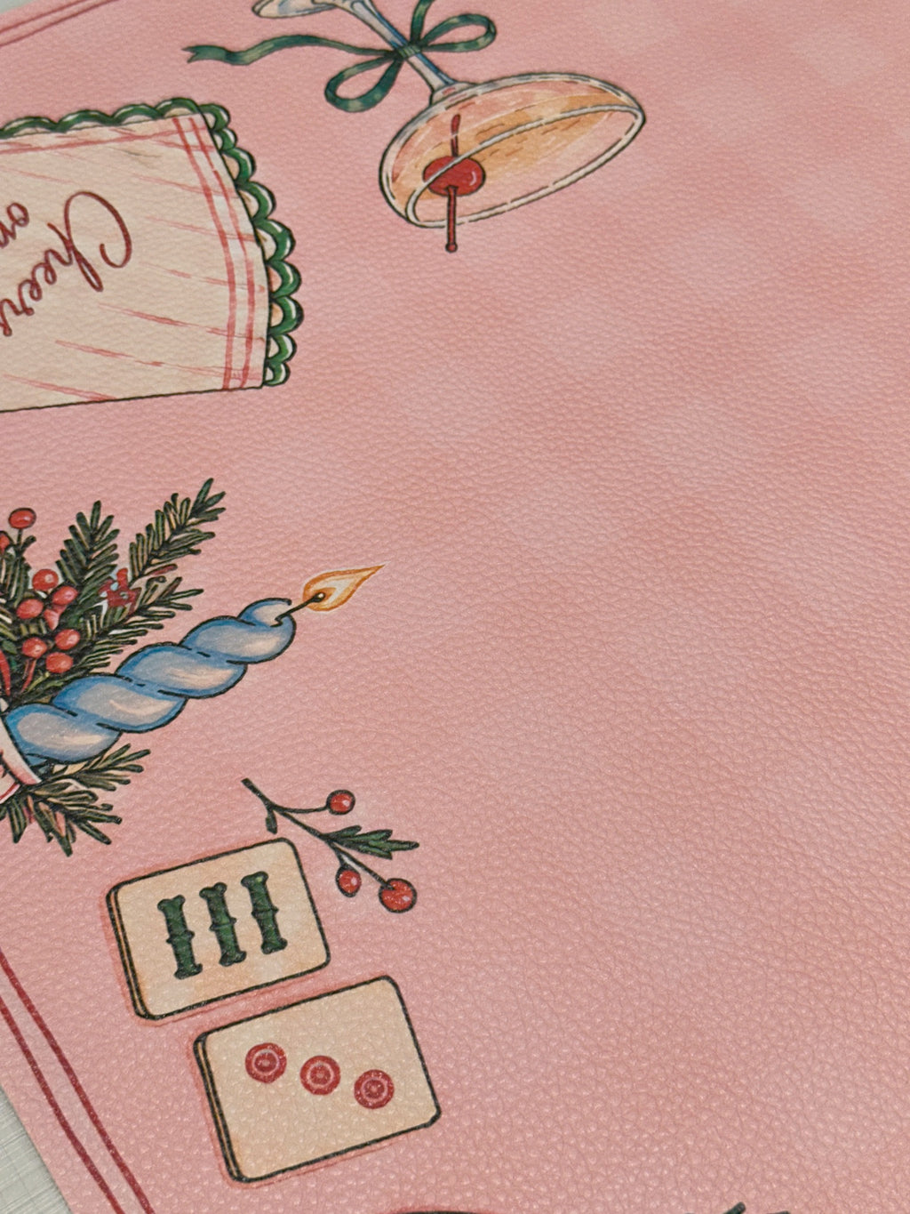 Textured vegan leather surface showing a blue candle, Mahjong tiles and a cocktail glass on the pink Merry Mahj mat