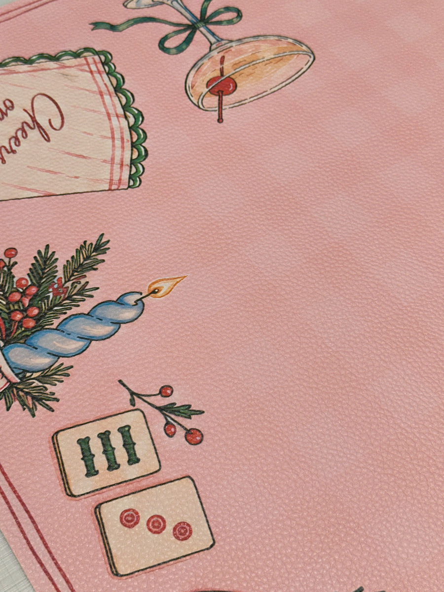 Textured vegan leather surface showing a blue candle, Mahjong tiles and a cocktail glass on the pink Merry Mahj mat