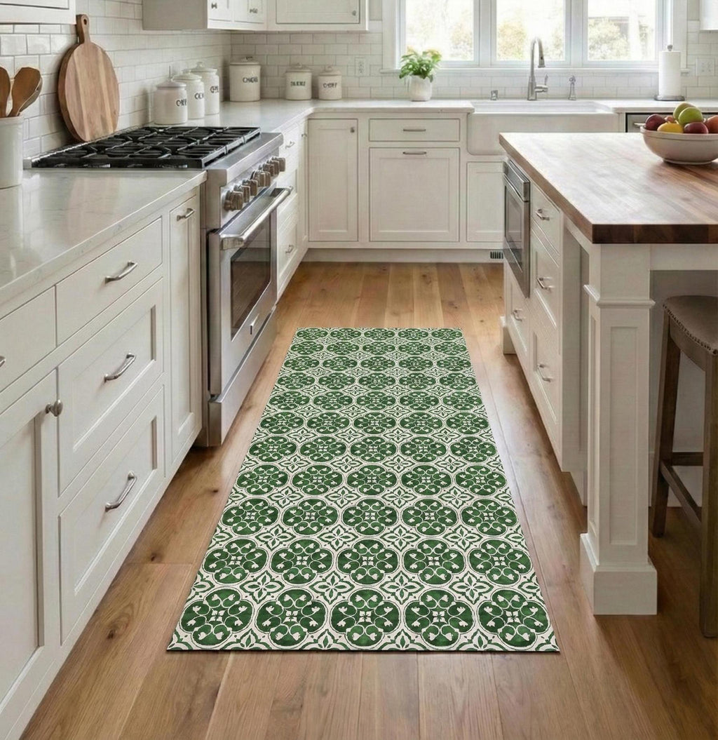 May include: A green and white patterned runner rug in a kitchen setting. The rug features a repeating floral design and is placed on a hardwood floor. The kitchen has white cabinets and stainless steel appliances.