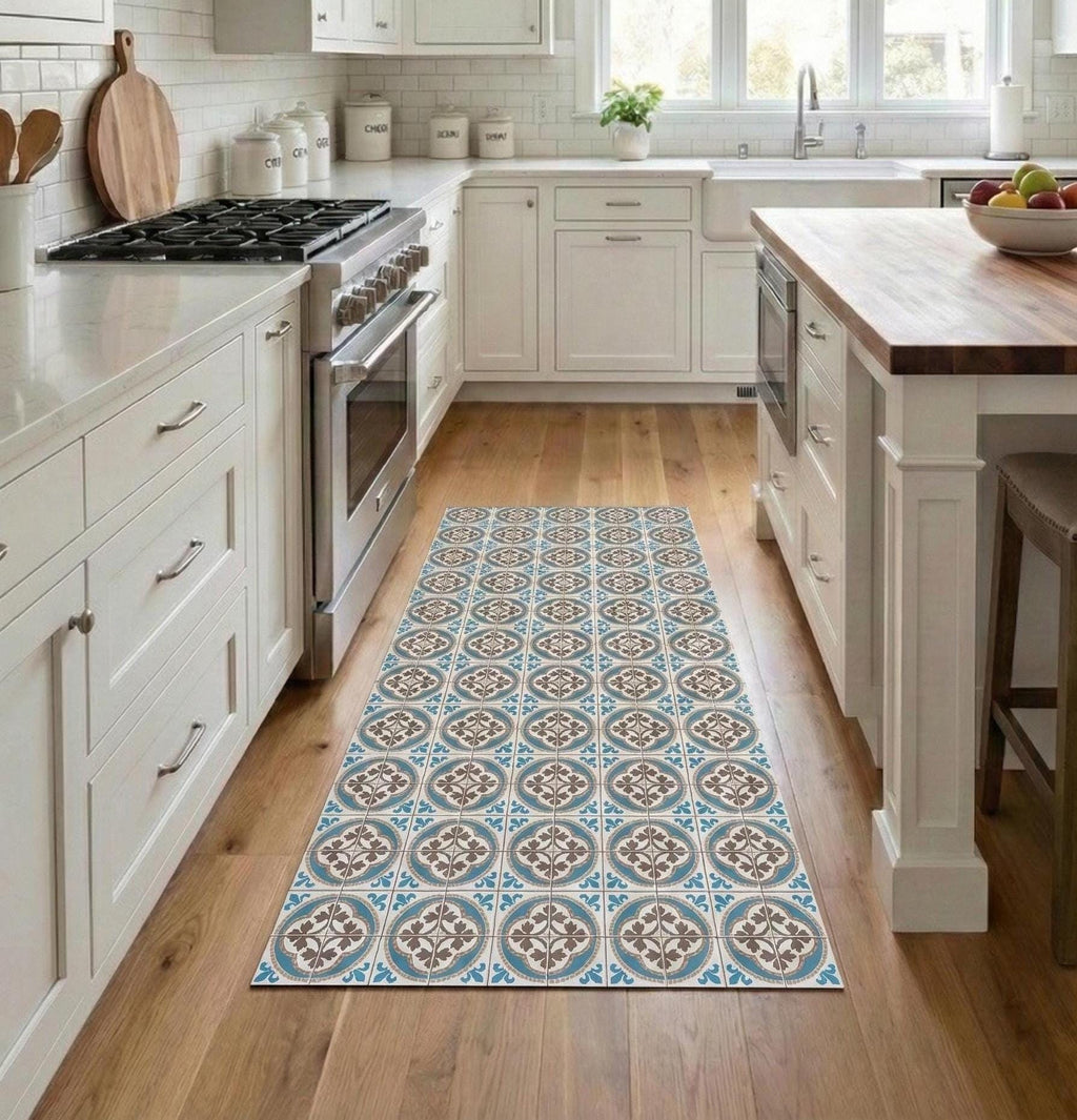 May include: A rectangular kitchen rug with a repeating pattern of blue, brown, and cream-colored tiles. The rug is placed on a hardwood floor in a kitchen with white cabinets and stainless steel appliances. The rug adds a decorative element to the kitchen.