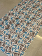 May include: A patterned floor covering featuring a repeating design of brown floral motifs within blue and white circular frames. The design is set against a white background with blue accents, creating a vintage aesthetic.