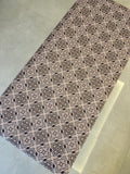 May include: A rectangular patterned fabric with a repeating geometric design in shades of brown, beige, and burgundy. The pattern is a symmetrical arrangement of shapes, creating a visually appealing surface. The fabric is likely used for home decor or crafting.