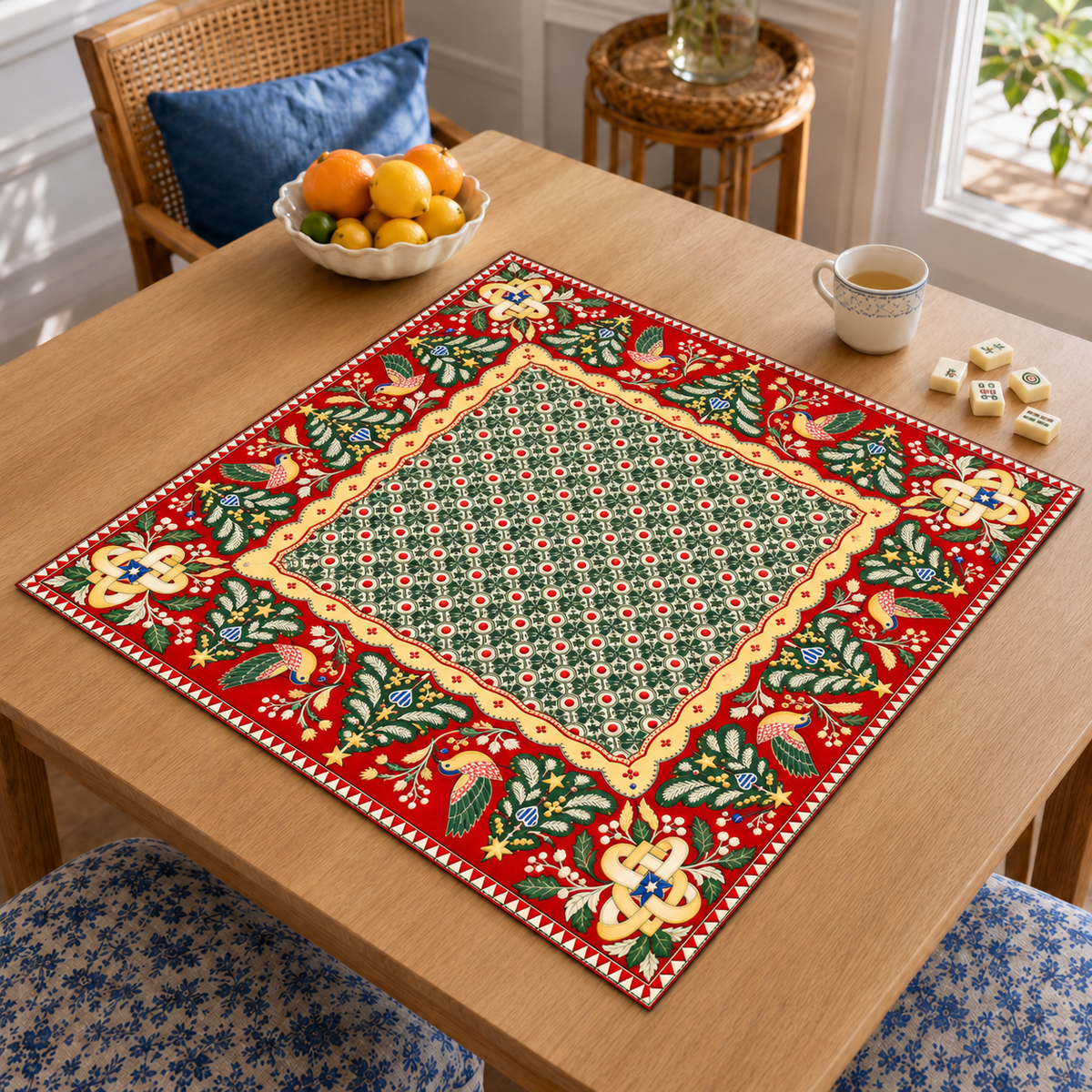 Angled table view of the Christmas Mahjong mat with green geometric center, red folk art border, stylized birds and Christmas trees