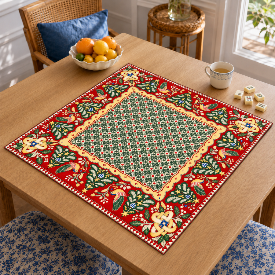 Angled table view of the Christmas Mahjong mat with green geometric center, red folk art border, stylized birds and Christmas trees
